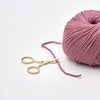 Pink skein of yarn with a pair of gold scissors on a white background