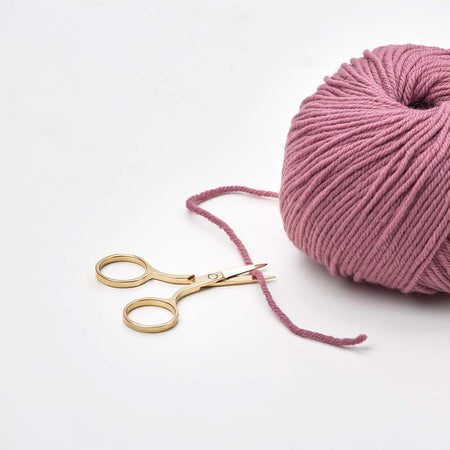 Pink skein of yarn with a pair of gold scissors on a white background