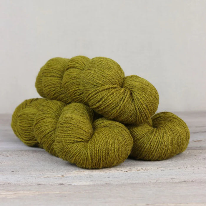 Five skeins of green yarn stacked on a wooden surface with a light gray background