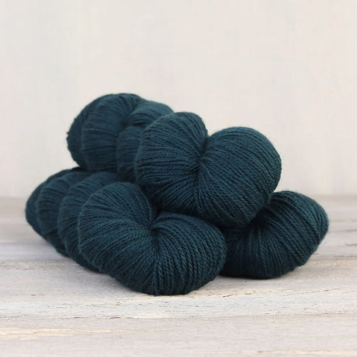 Four skeins of dark teal yarn on a light wooden surface with a neutral background
