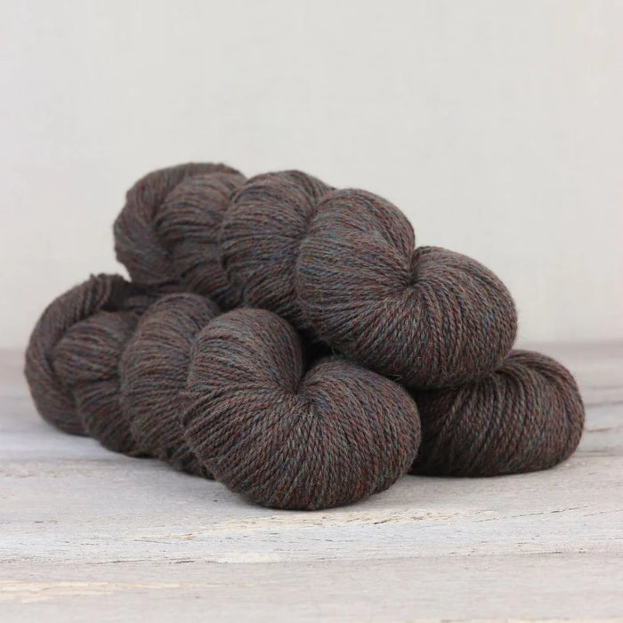 Dark brown yarn skeins on a light wooden surface with a white background