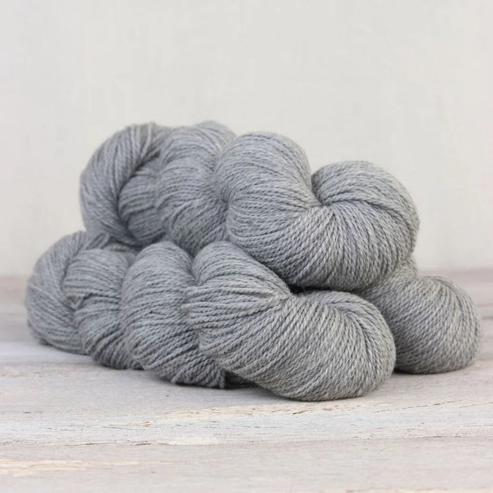 Three skeins of light grey yarn on a light wooden surface with a neutral background