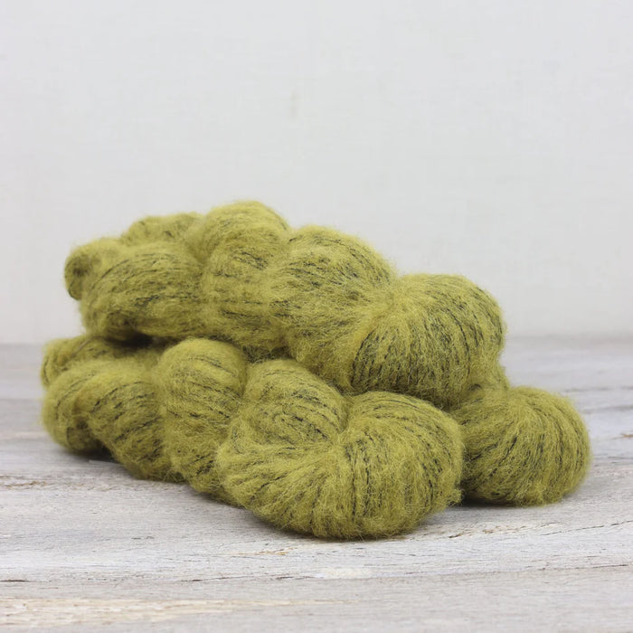 Green yarn skeins on a wooden surface with a light gray background