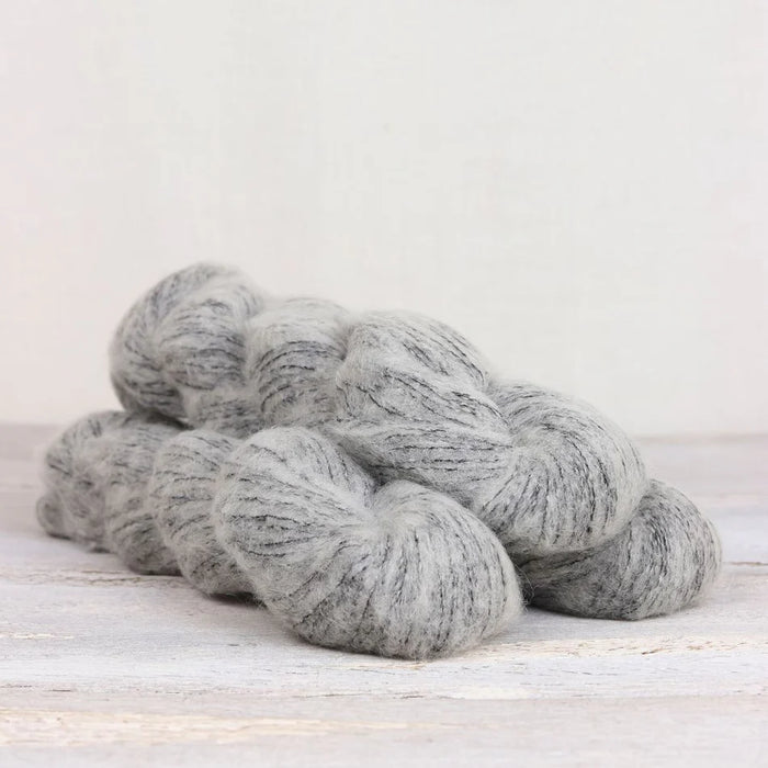 Gray yarn skeins on a light wooden surface with a white background