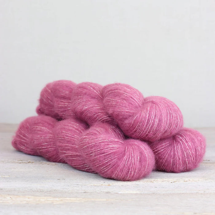 Pink yarn skeins on a light wooden surface with a white background
