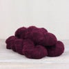 Burgundy yarn skeins on a light wooden surface with a white background