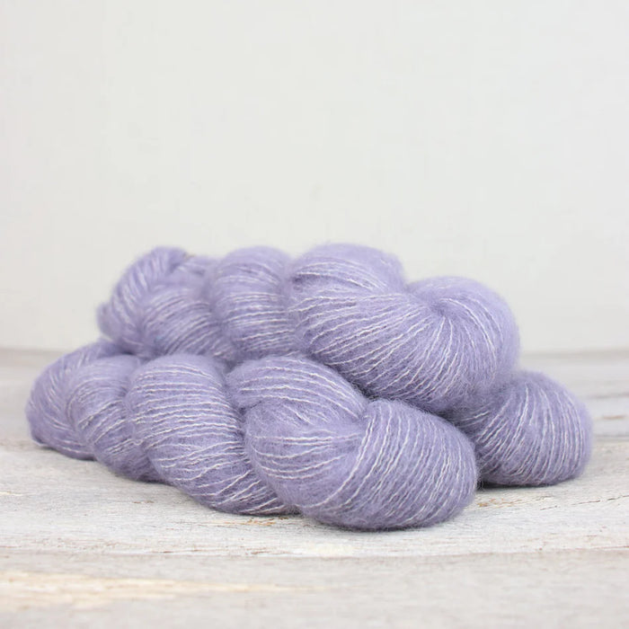 Purple yarn skeins on a light wooden surface with a white background