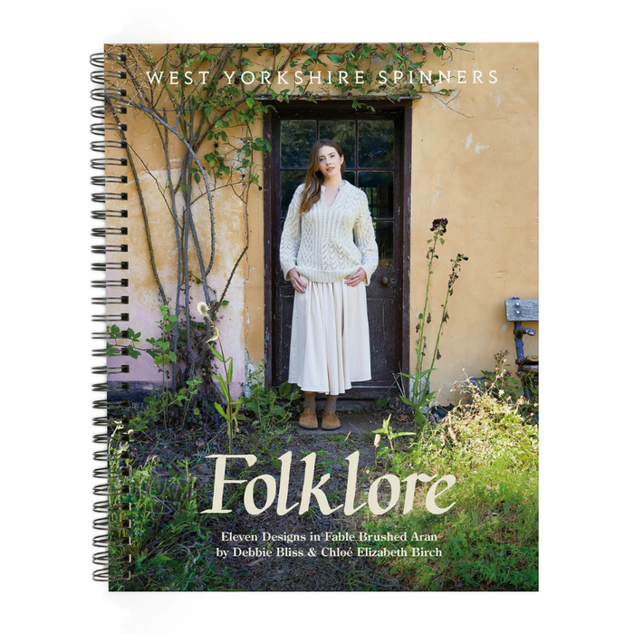 Book cover of 'Folklore' by West Yorkshire Spinners with a woman in a white knitted jumper standing in front of a door.