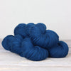 Three skeins of dark blue yarn on a light wooden surface with a neutral background