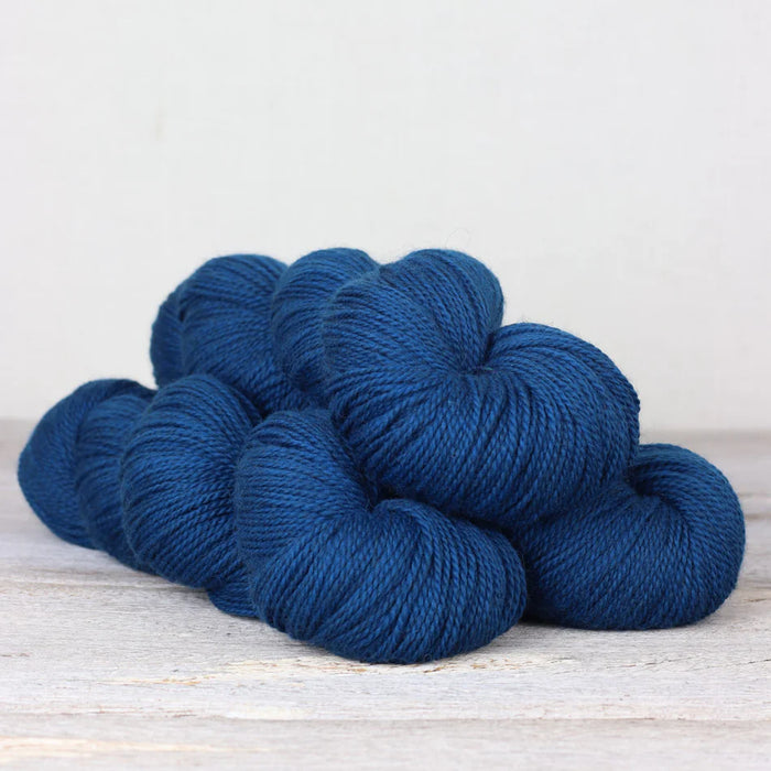 Three skeins of dark blue yarn on a light wooden surface with a neutral background