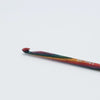 A single crochet hook with a multicolor painted handle and a red tip, photographed on a plain light gray background. White text on the handle.
