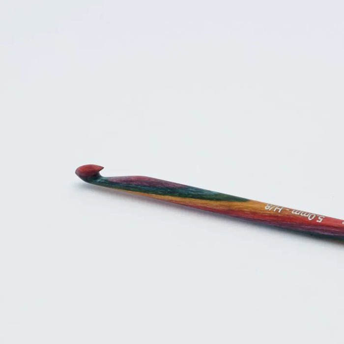 A single crochet hook with a multicolor painted handle and a red tip, photographed on a plain light gray background. White text on the handle.